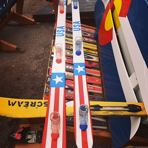 Two 3 person shot skis with American flag design on a wooden surface.