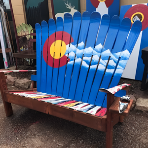 Reclaimed ski Adirondack loveseat with hand-painted Colorado flag and mountain scene on the backrest, colorful mixed ski seat, and ski pole armrests, set on a wood frame
