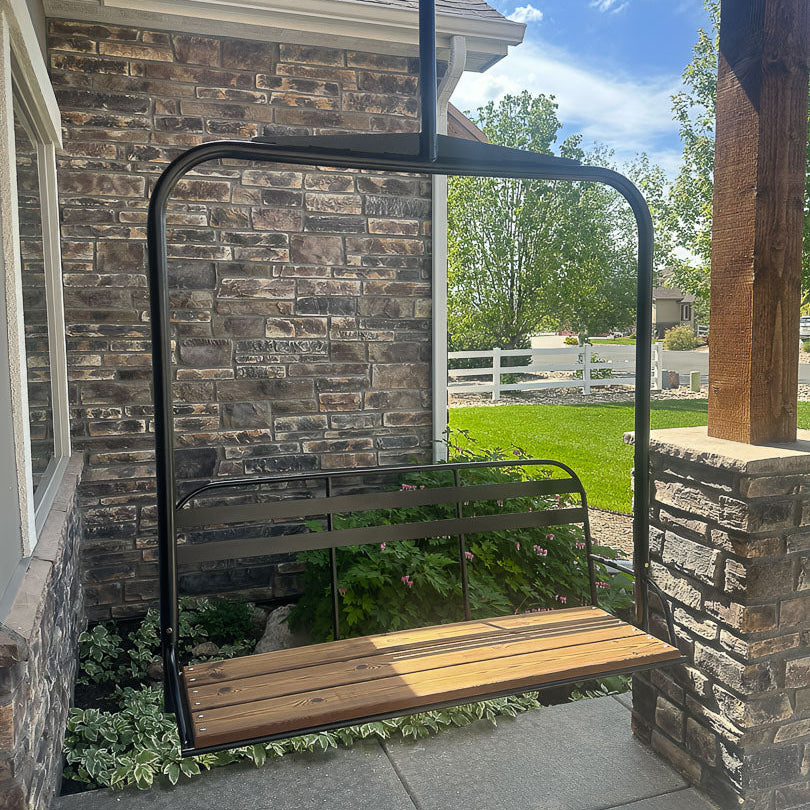 Ski lift swing with black powder coat hanging from a porch with stone wall and greenery in the background