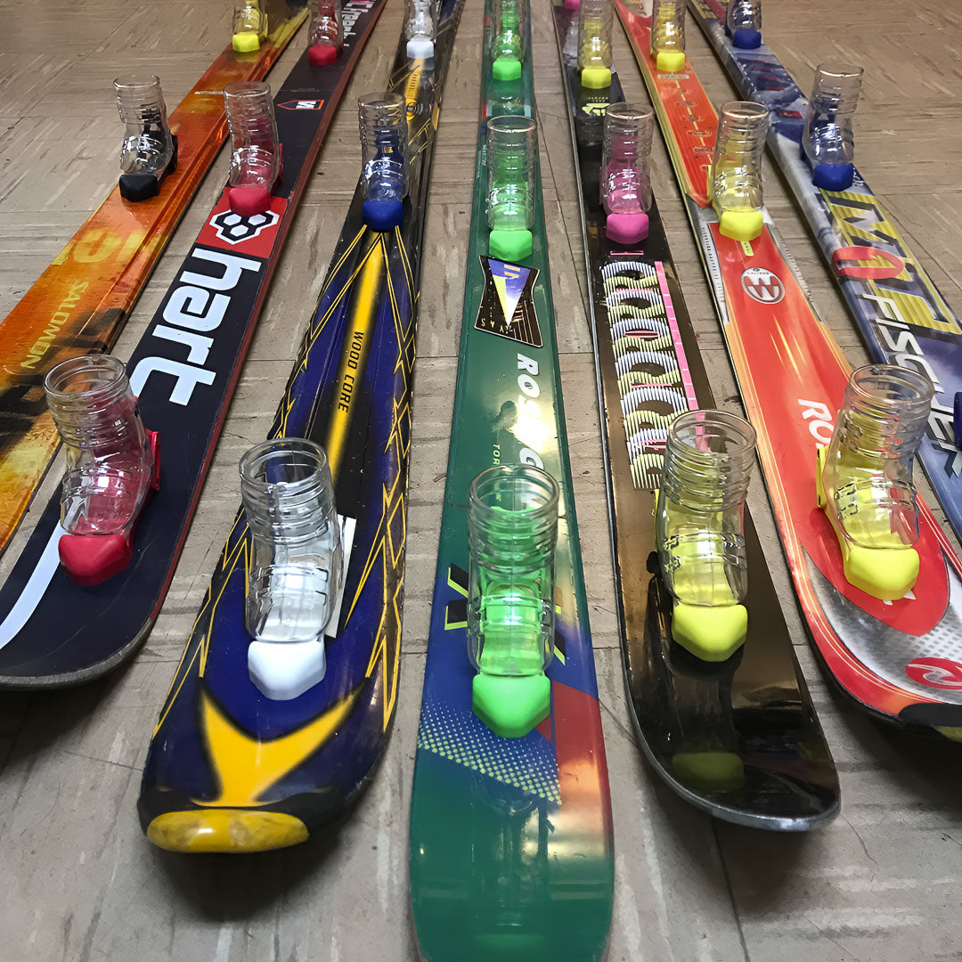 Multiple pairs of skis with shot ski boots on a floor