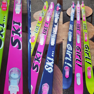 Colorful hand painted shoskis with 'Ski Like a Girl!' text on a wooden surface. 