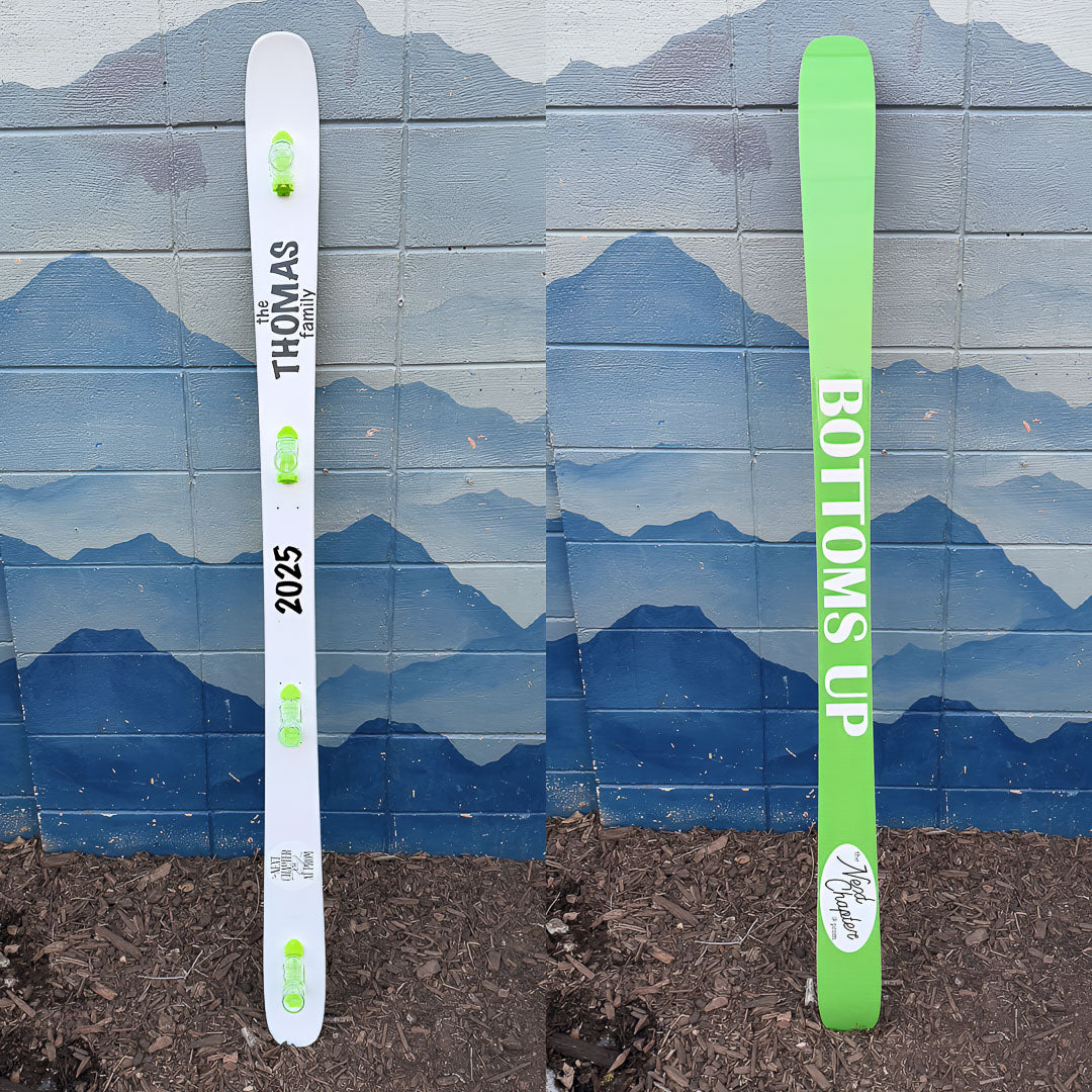 Hand painted family themed shot ski painted on both sides. The top is painted white with green shot glasses and the bottom is painted light green with white "Bottoms Up" text.