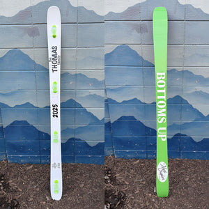 Hand painted family themed shot ski painted on both sides. The top is painted white with green shot glasses and the bottom is painted light green with white "Bottoms Up" text.