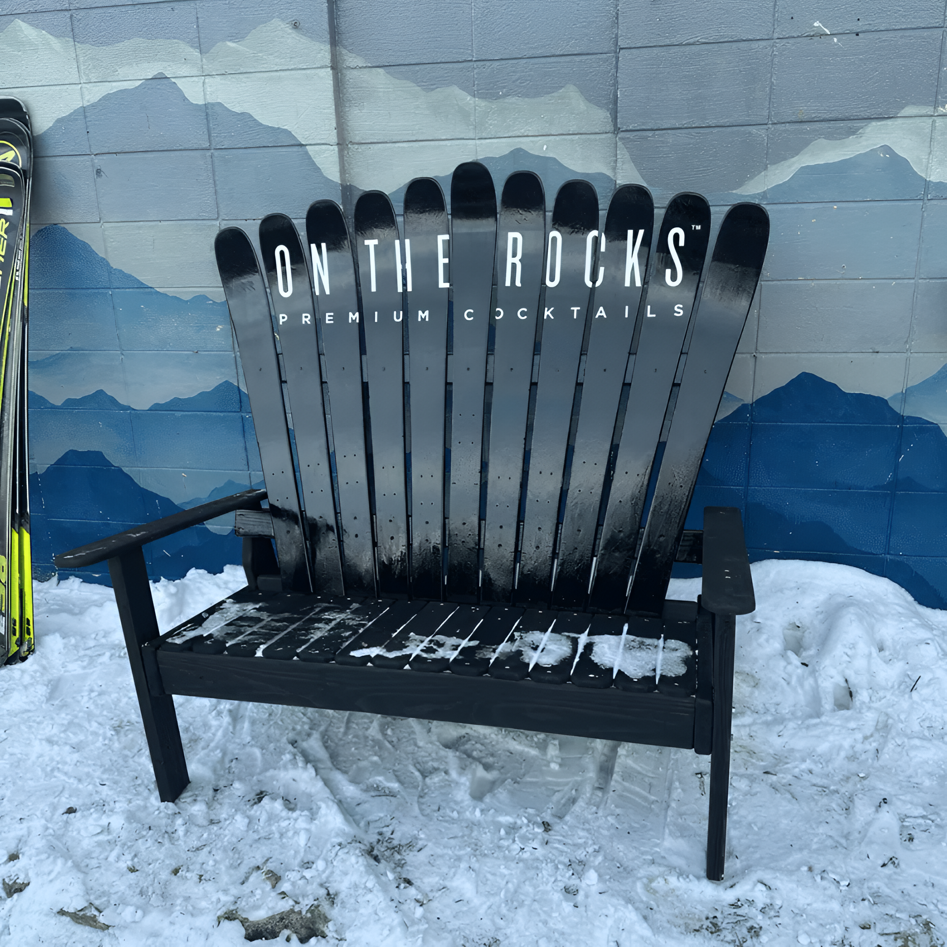 Custom branded reclaimed ski Adirondack loveseat with On The Rocks Premium Cocktails logo on all-black backrest and wood frame